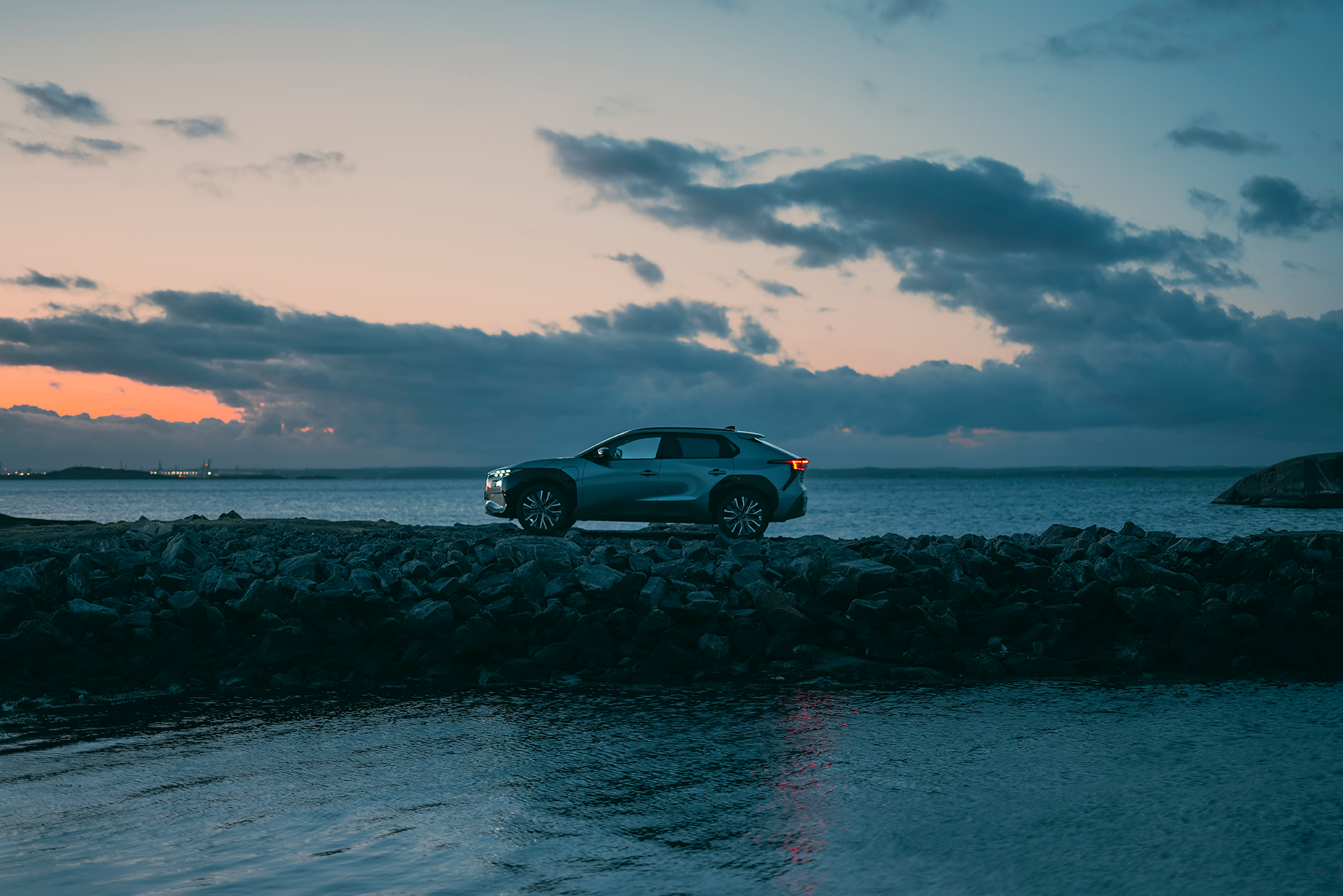 Subaru Solterra pargitud kivisel mererannikul päikeseloojangu ajal.